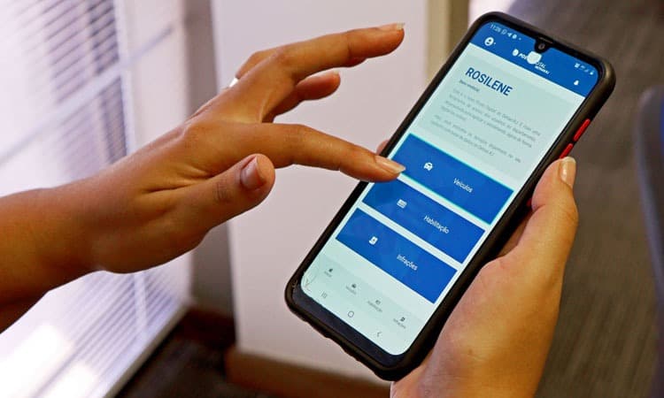 Imagem de uma mão com um celular mexendo no aplicativo do Detran-RJ